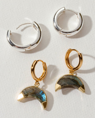 Two pairs of huggie earrings, one silver the other gold with labradorite moon charms by Luna Norte Jewelry.