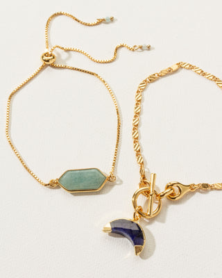 Two gold bracelts, one with a green gemstone hexagon amazonite charm and the other a sapphire moon charm