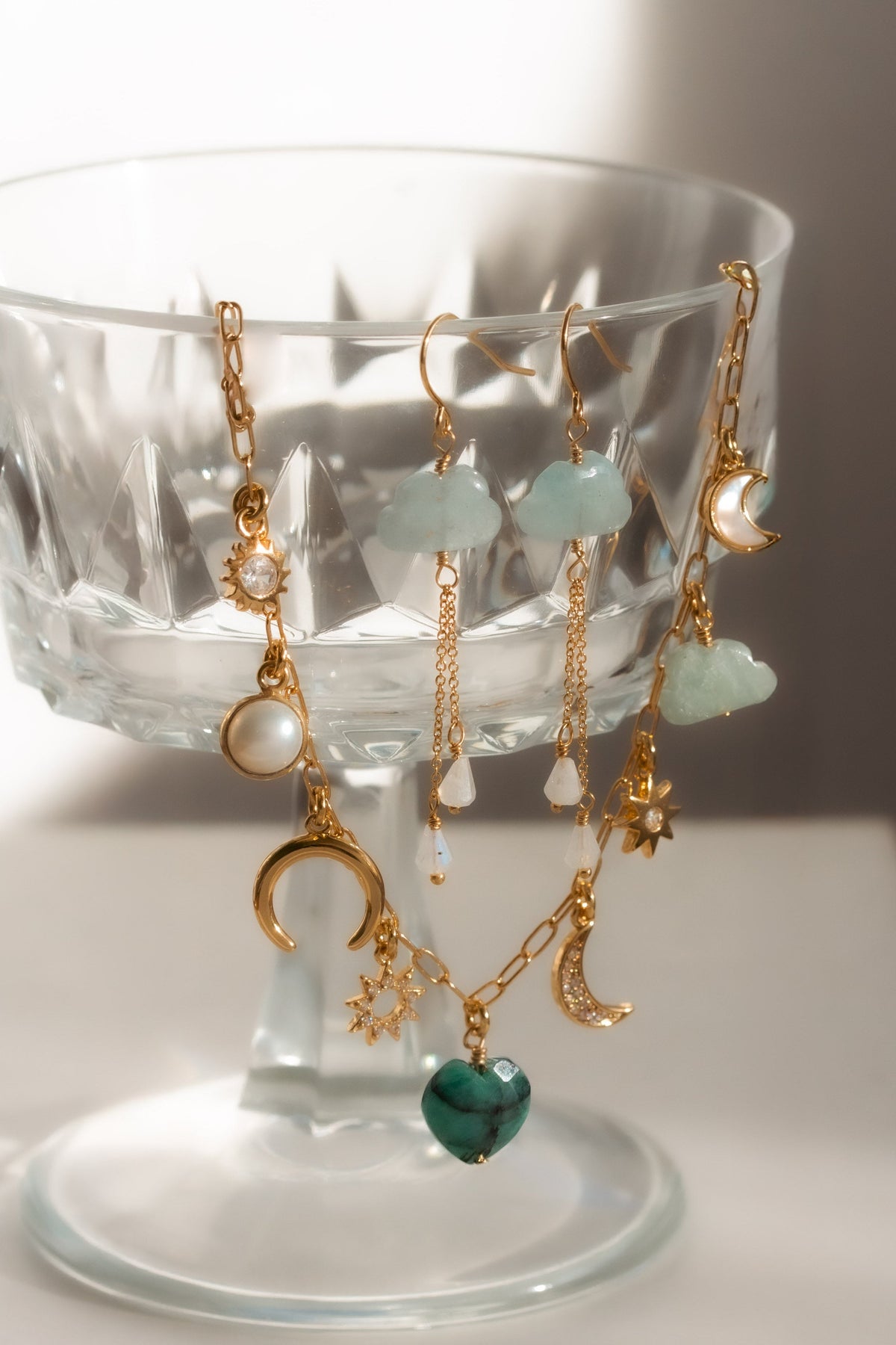 Charm Necklace with gemstones and gold chainsand gemstone earrings on a glass stand.