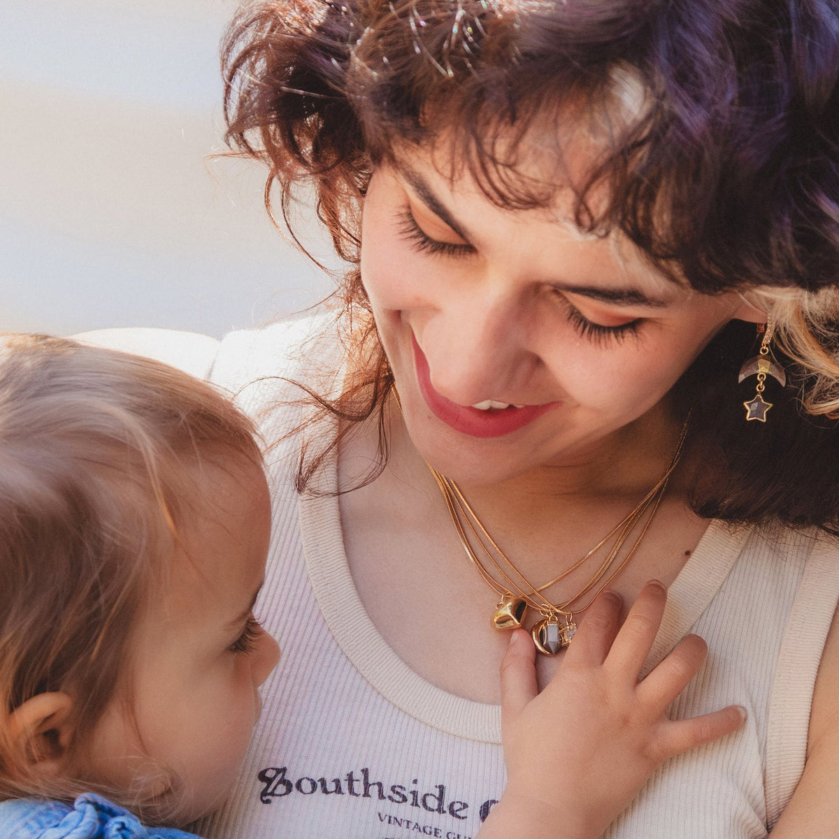 woman holding a child, both smiling, while the child plays with the woman's necklace set