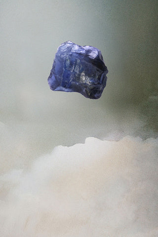 Raw blue sapphire gemstone on a textured white and gray background