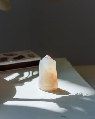 Semi Translucent agate crystal mini tower on a light surface with a dark background.