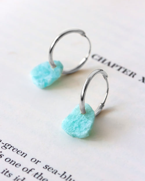 A pair of silver-plated hoop earrings with raw-edge amazonite gemstones on book page.