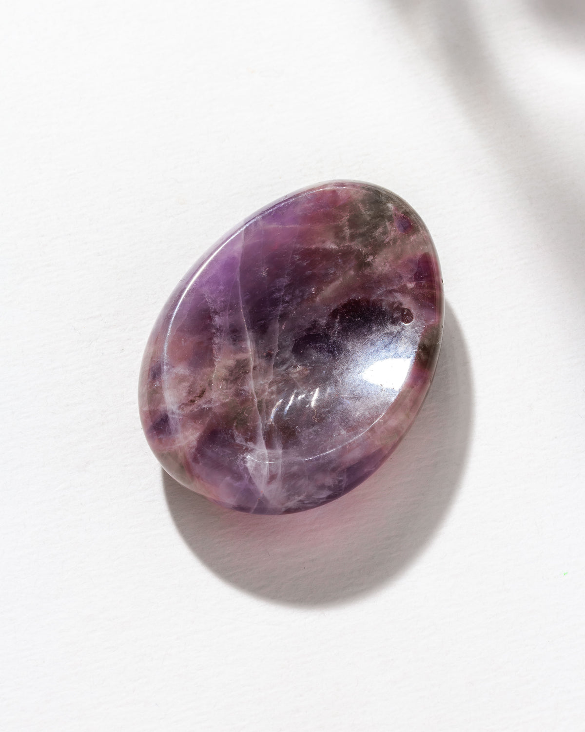 A smooth amethyst stone with a slight indent, placed on a white surface.
