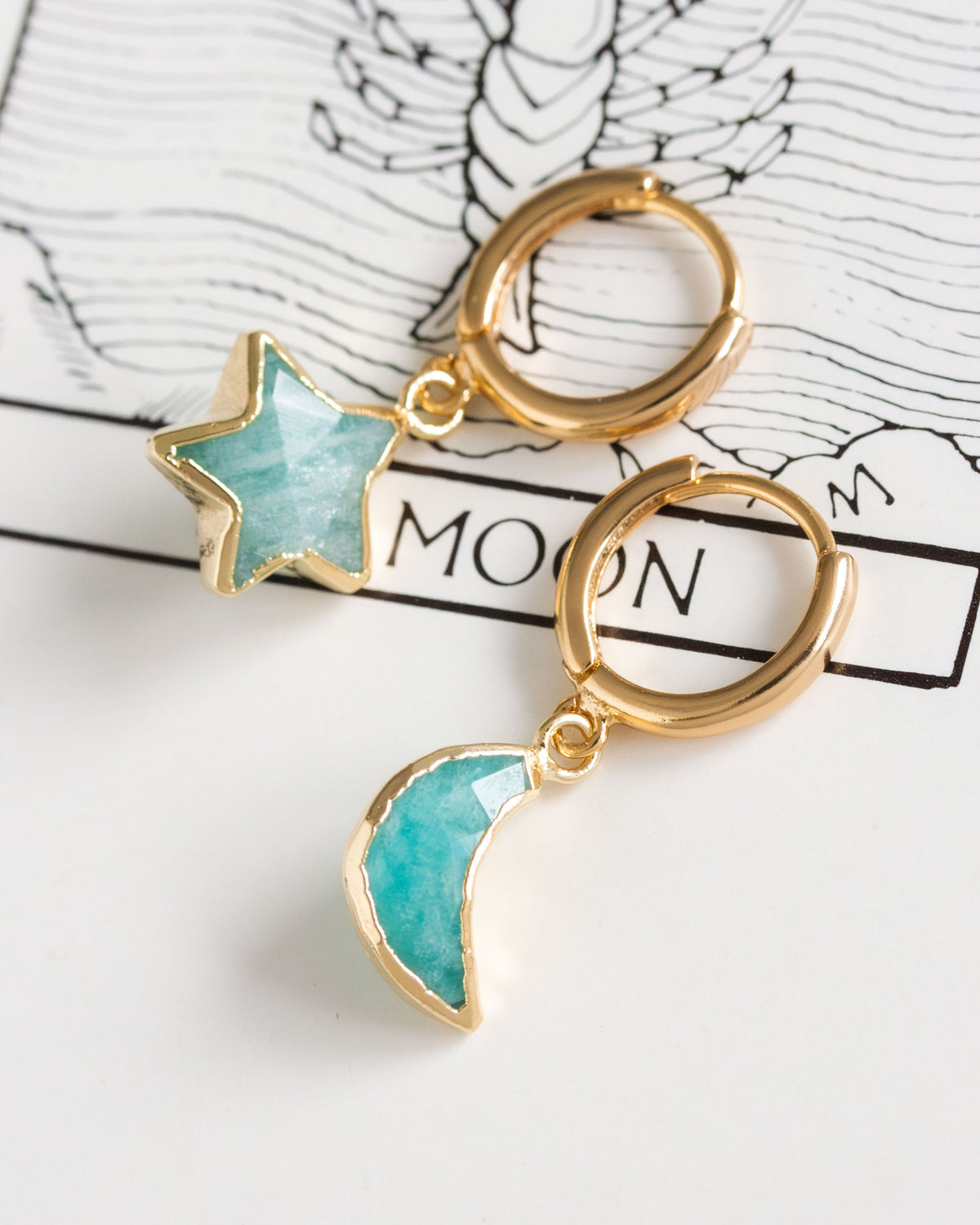 Pair of mismatched gold huggie hoop earrings with aquamarine star and moon charms