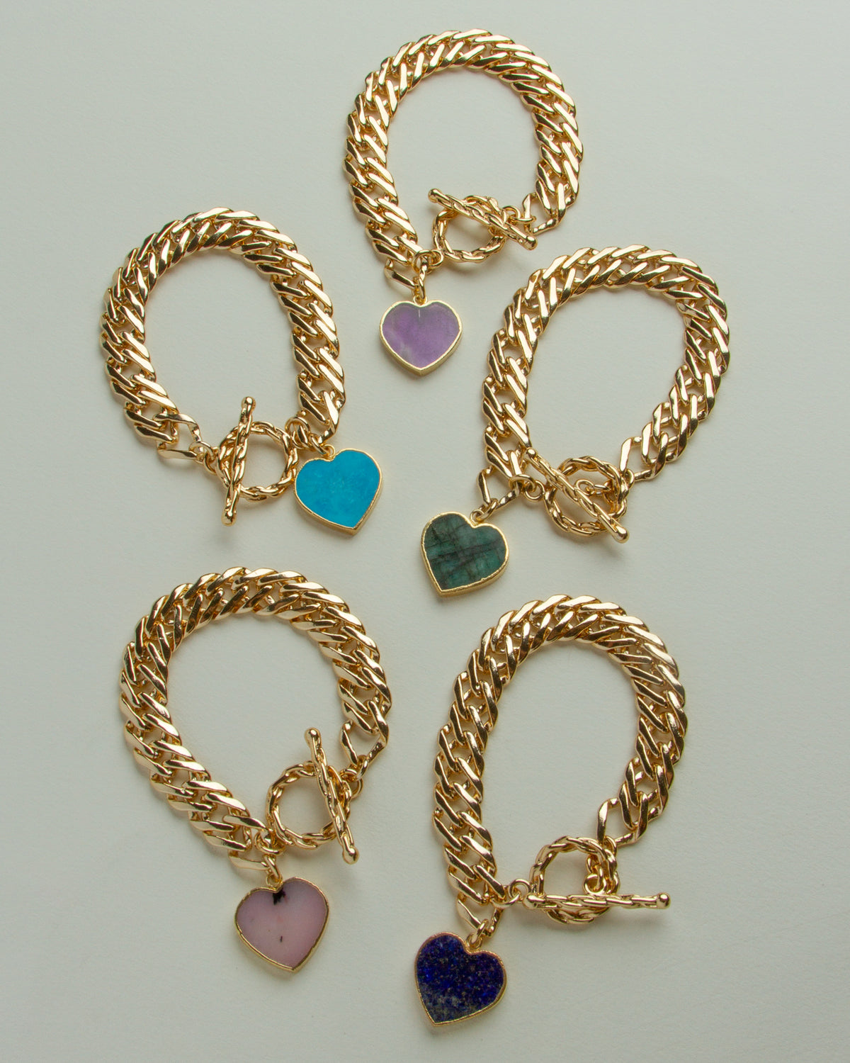 Five gold chain toggle clasp bracelets with heart charms in: purple, turquoise, green, pink and blue