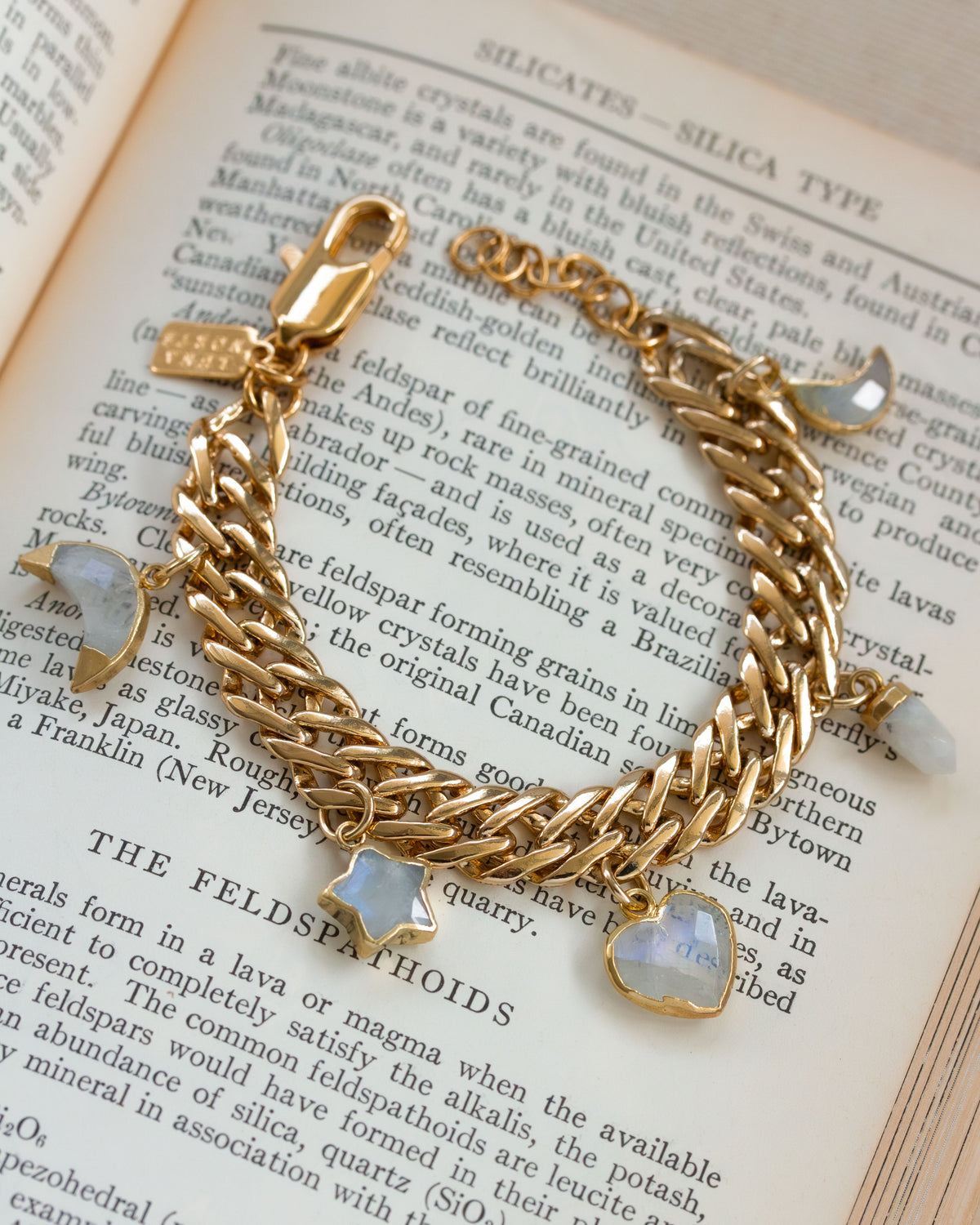 Gold bracelet with moonstone heart, crescent moon, star, and crystal charms, on a book page.