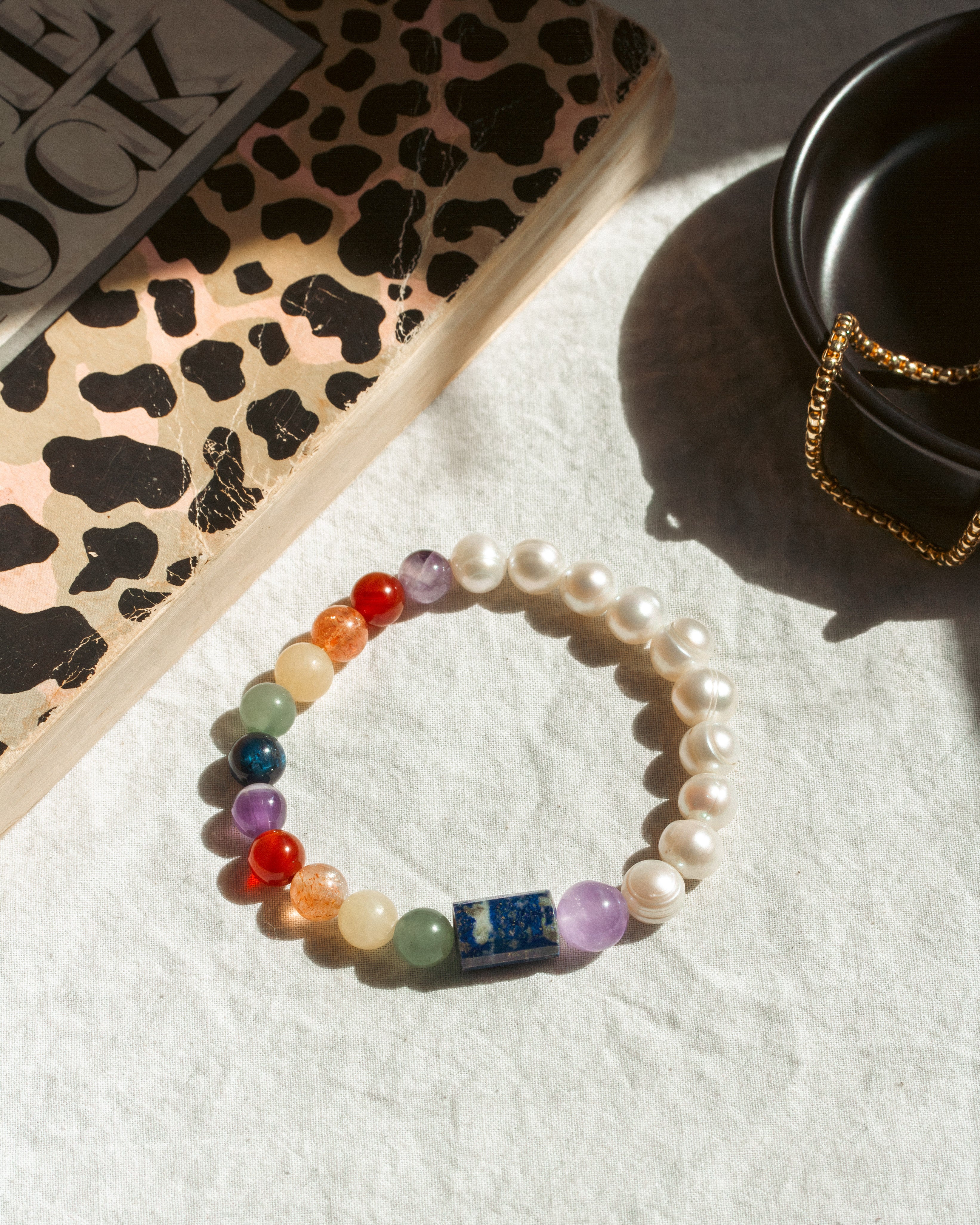 Colorful beaded bracelet on a white surface with a leopard print book and black container