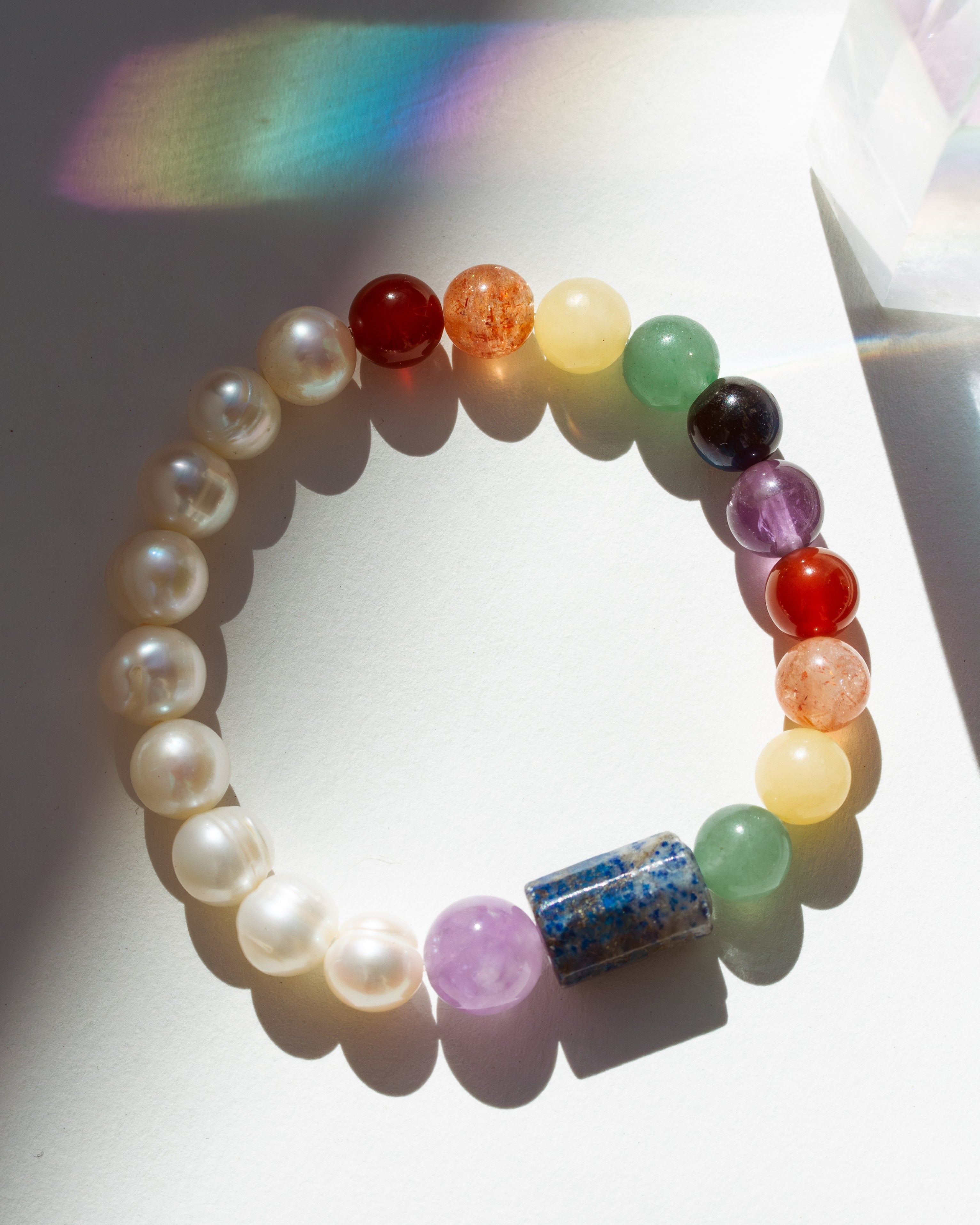 Multicolored beaded bracelet on a white surface with a rainbow shadow