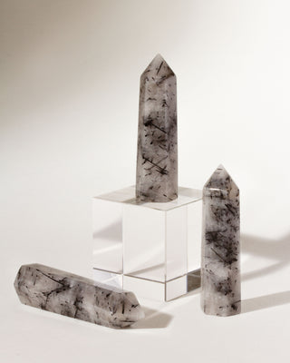 A collection of tourmalinated quartz crystal towers displayed on a white surface, with varying angles showing the hexagonal shape and the inclusions within the stones.