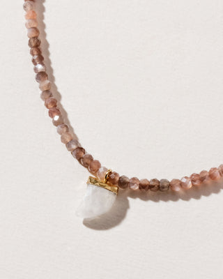 A collar-length necklace with coffee moonstone beads and a carved rainbow white moonstone shark-tooth shaped charm, displayed against a soft background.