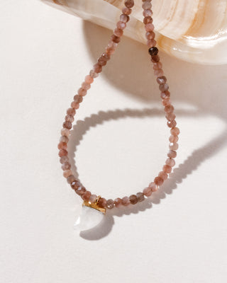 A collar-length necklace with coffee moonstone beads and a carved rainbow white moonstone shark-tooth shaped charm, displayed against a soft background.