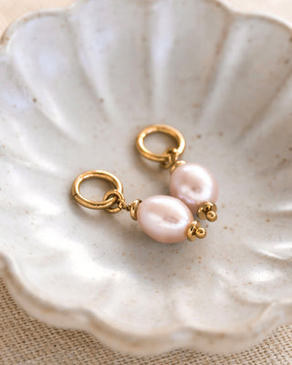 Pink pearl and gold interchangeable earring pair laying on a white shell shaped dish.