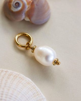 Single pearl gold plated hoop earring on a neutral surface near seashells.