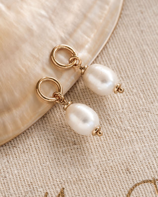 A pair of pearl hoop earring charms placed on a textured surface.