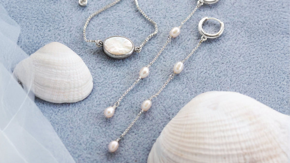 Pearl earrings with silver clasp on a blue surface with seashells