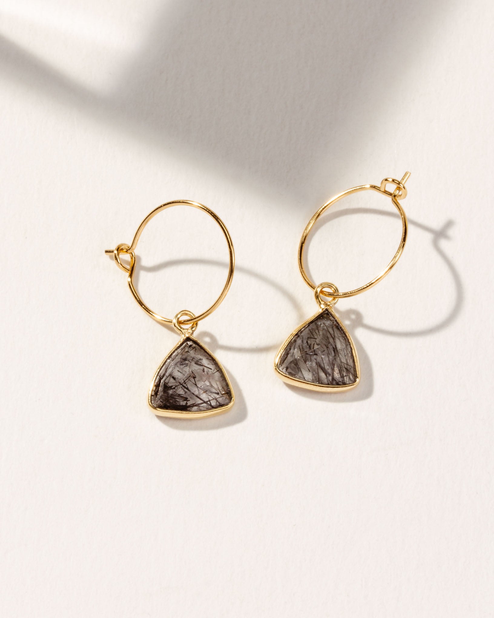 Gold hoop earrings with triangular Tourmalinated Quartz pendants on a light background