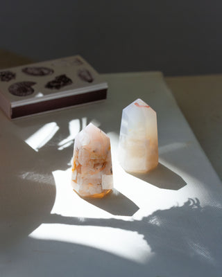 Two polished agate gemstone towers with a faceted design, displaying internal patterns, placed on a flat surface with natural light casting on them.