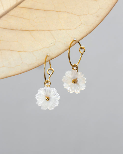 Pair of gold hoop earrings with white mother-of-pearl shell daisy designs attached to the hoops