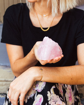 Person holding a pink crystal while wearing a black shirt with floral patterns.
