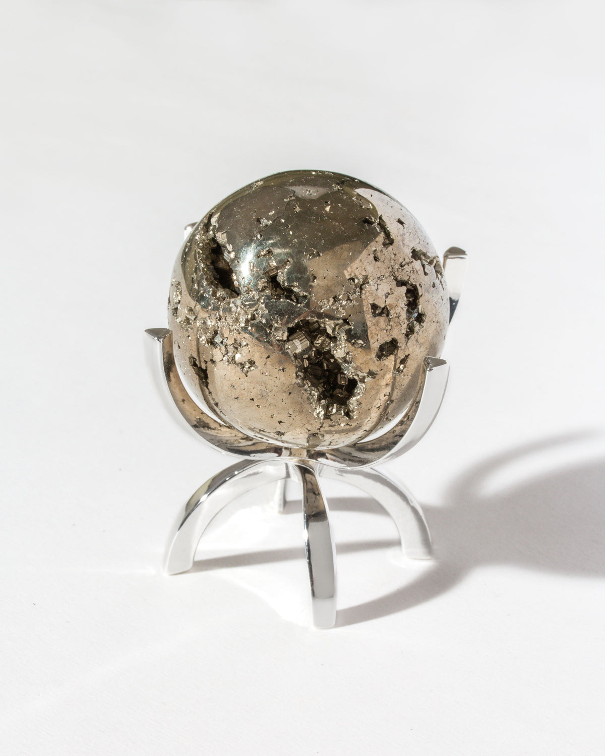 Shiny pyrite sphere with rough patches sitting on a silver, four-pronged display stand.