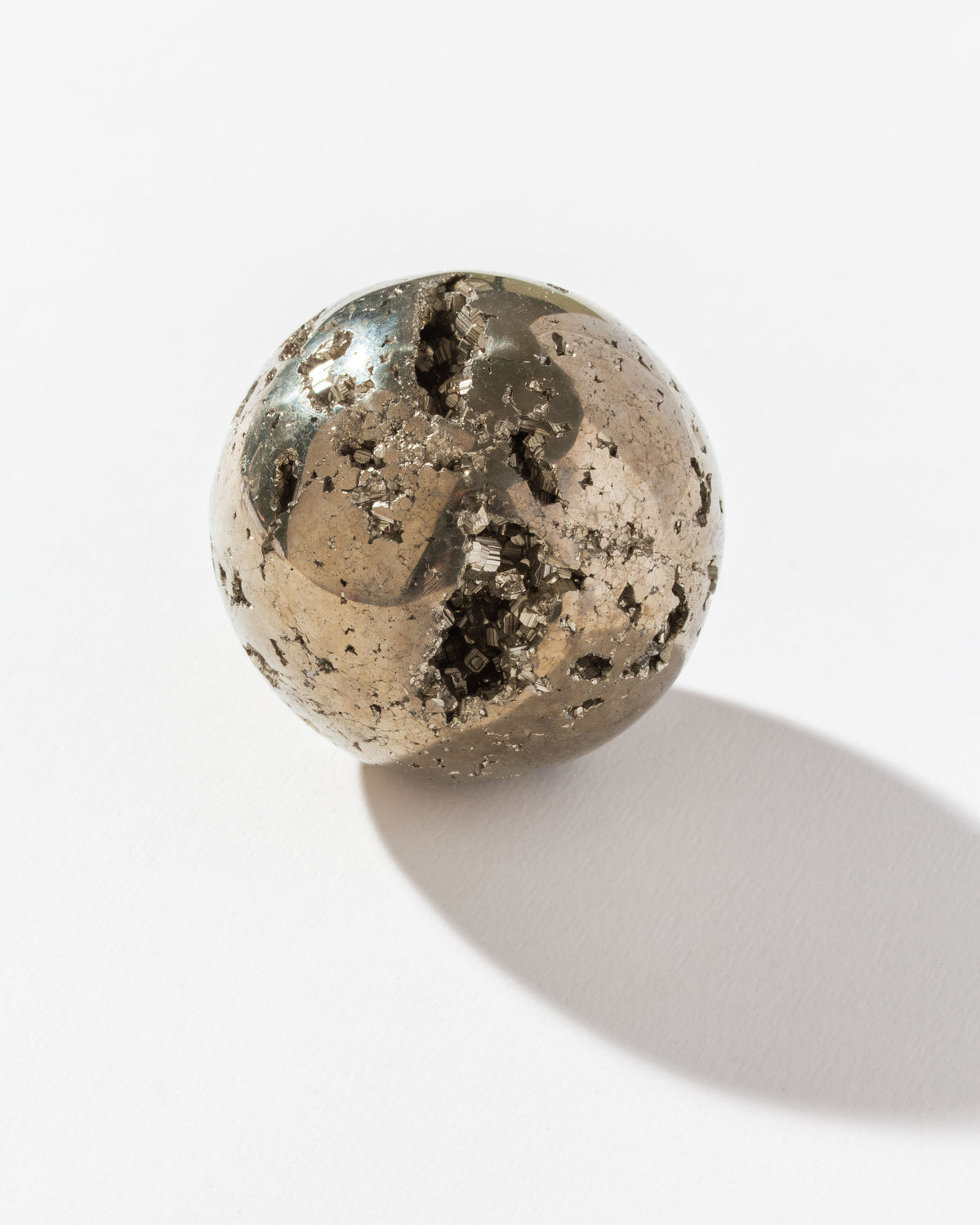 Polished pyrite sphere with textured surface and visible inner crystals, resting on a white surface.