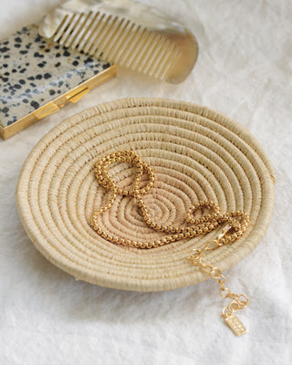 Beige woven basket with gold jewelry on a light background