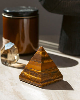 Tiger's eye crystal pyramid sitting on a white table, with curios in the background.