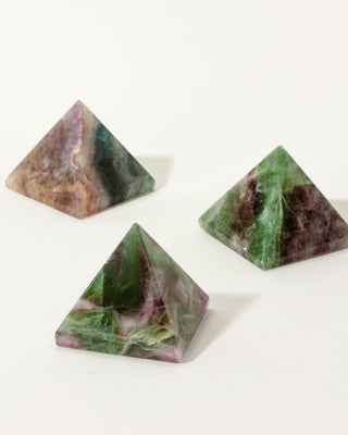 Three pyramid-shaped green and purple tiger's eye marbled stones on a white background