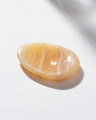A smooth calcite stone with a slight indent, placed on a white surface.