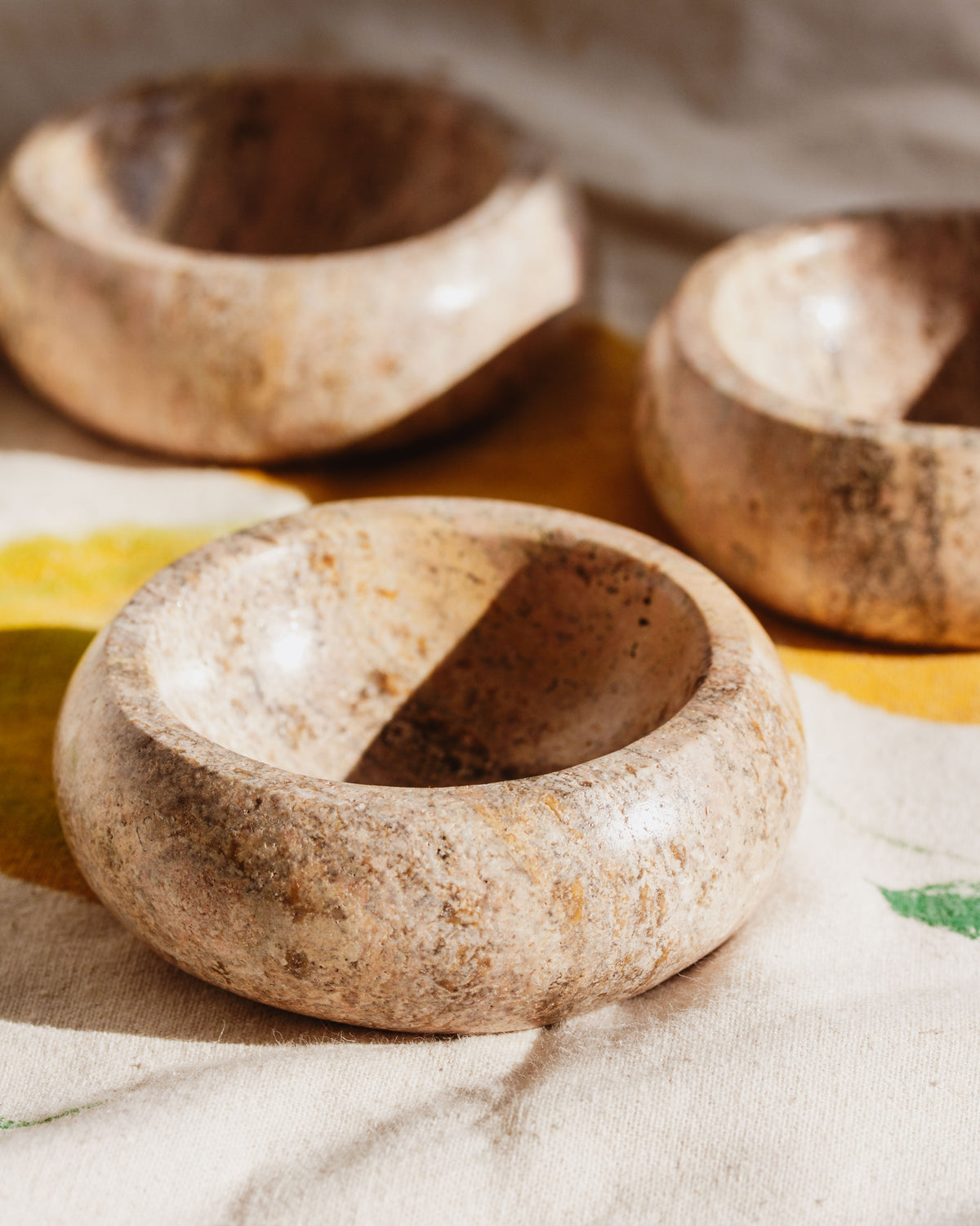 Three calcite jewelry catchall bowls on a floral motif cloth.