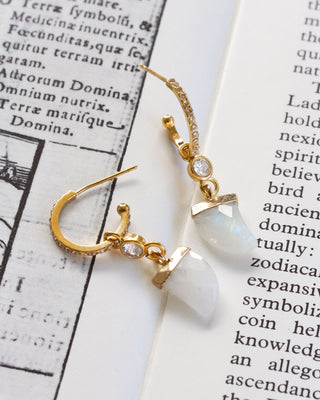 Gold hoop earrings with moonstone shark tooth shaped stones on a book page background