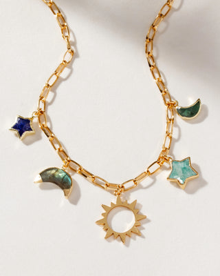 A gold-plated charm necklace with a paperclip chain design, featuring multicolored gemstone charms in the shapes of moons and stars, and a central gold sun pendant.