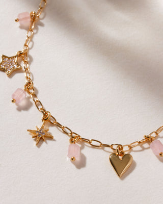 Closeup of gold charm necklace with rose quartz, gold, and cz charms in heart, pendant, and star shapes.