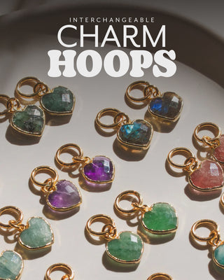 Gold charm hoops with heart gemstone pendants on a light background, labeled 'Interchangeable Charm Hoops'.