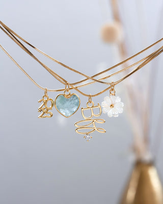 Layered gold necklaces with 2025, BFF, Aquamarine heart, and mother-of-pearl floral charms on a light gray background