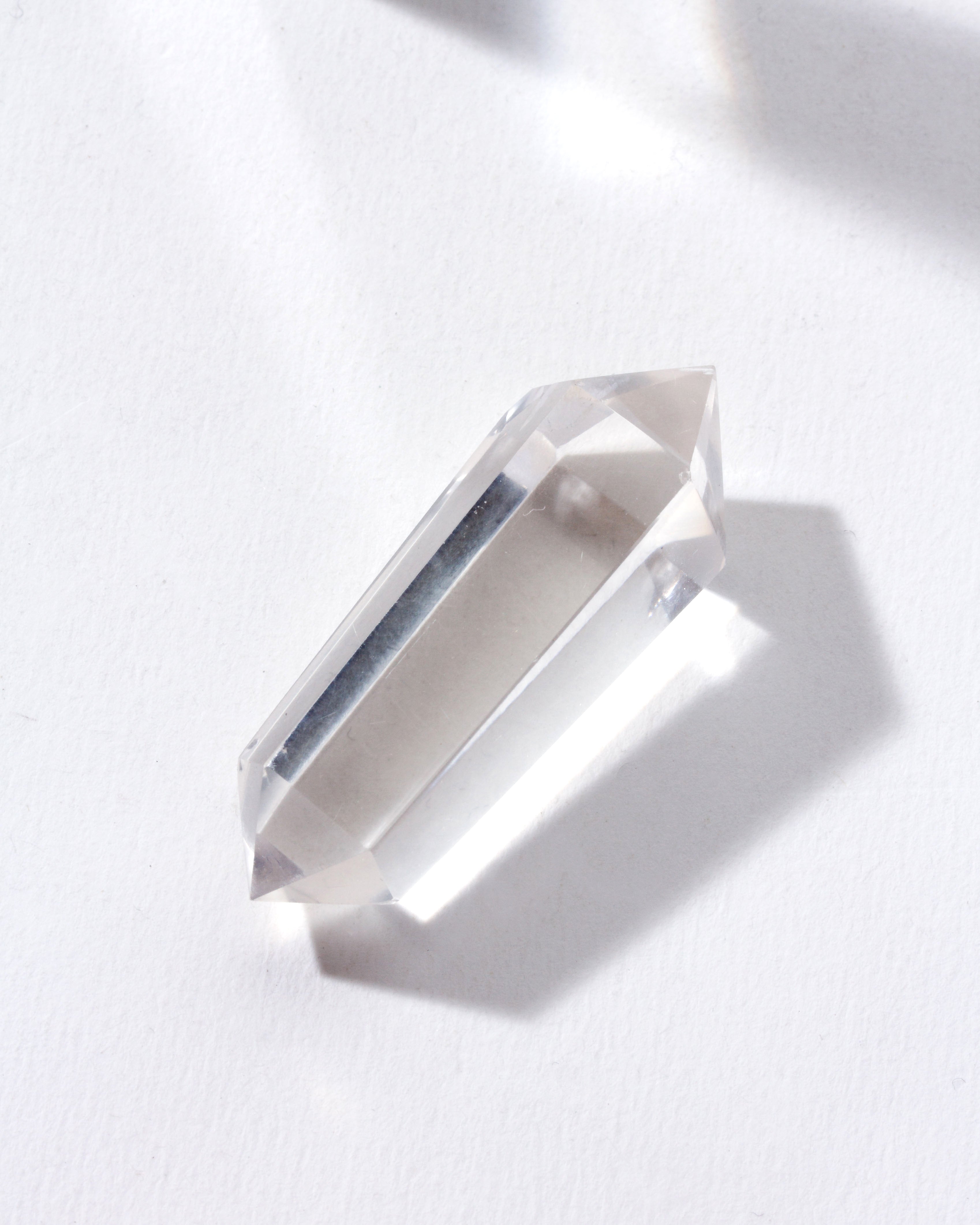 A clear quartz double pointed crystal placed on a white surface.