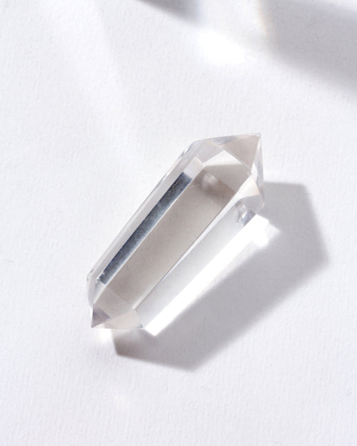 A clear quartz double pointed crystal placed on a white surface.