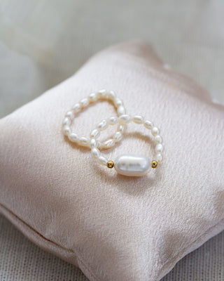 Pearl stretch ring with gold accents on a soft pink fabric pillow.