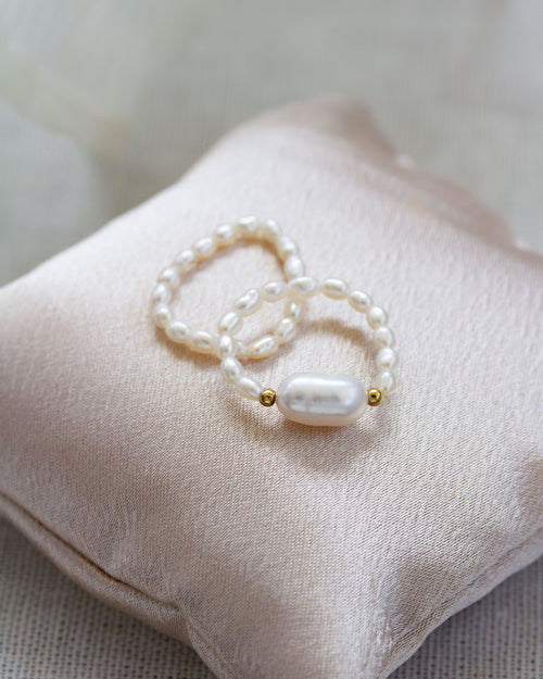 Pearl stretch ring with gold accents on a soft pink fabric pillow.