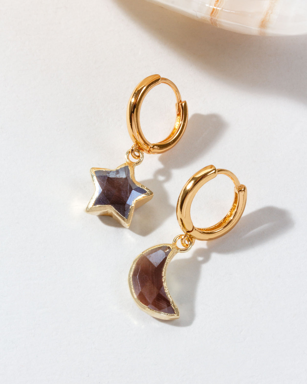 Pair of mismatched gold huggie hoop earrings with coffee moonstone star and moon charms