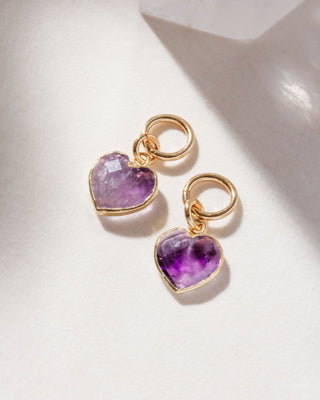 A pair of interchangeable hoop earring charms with heart shaped amethyst gemstone displayed on a white surface.