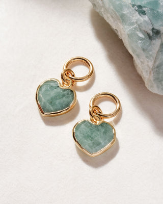 A pair of interchangeable hoop earring charms with heart shaped aquamarine gemstone displayed on a white surface.