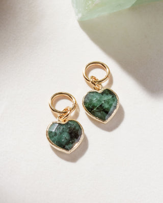 A pair of interchangeable hoop earring charms with heart shaped emerald gemstone displayed on a white surface.