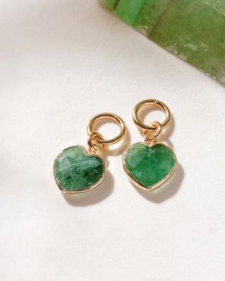 A pair of interchangeable hoop earring charms with heart shaped green strawberry quartz gemstones displayed on a white surface.