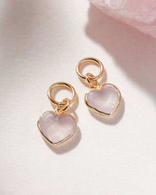 A pair of interchangeable hoop earring charms with heart shaped rose quartz gemstone displayed on a white surface.