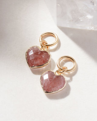 A pair of interchangeable hoop earring charms with heart shaped strawberry quartz gemstone displayed on a white surface.