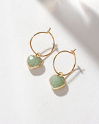 Gold hoop earrings with green aventurine heart gemstone charms on a white background
