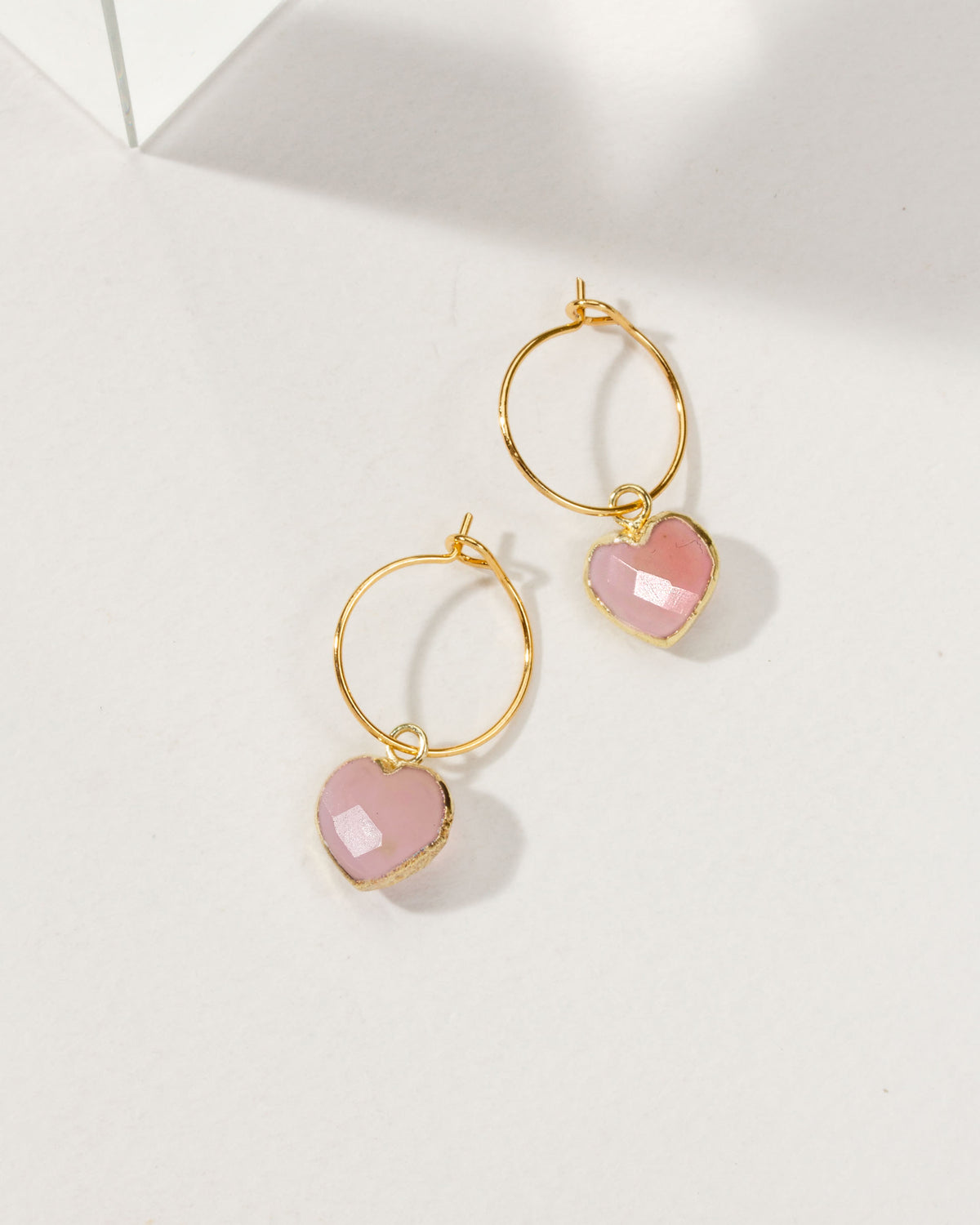 Gold hoop earrings with pink opal heart charms on a white background
