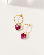 Gold hoop earrings with red ruby gemstones on a white background
